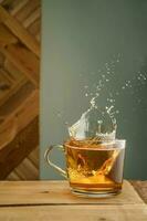 Transparent mug with tea and splashes on a green background. photo