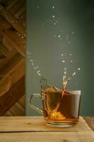 Transparent mug with tea and splashes on a green background. photo