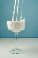 Milk pours into a beautiful crystal glass on a blue background and splashes around. photo