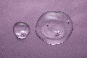 un gotas de transparente cosmético gel en un púrpura antecedentes. foto