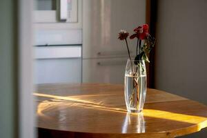 A bouquet in a transparent vase on a wooden table in the rays of the sun. photo