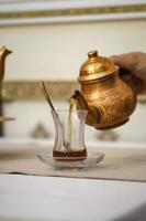 A man's hand pours tea into a Turkish cup from a copper teapot. photo