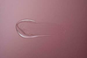 Drop of cosmetic transparent gel on a pink background. The texture of the serum, heir gel or hyaluronic booster. photo