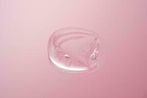 Drop of cosmetic transparent gel on a pink background. The texture of the serum, heir gel or hyaluronic booster. photo