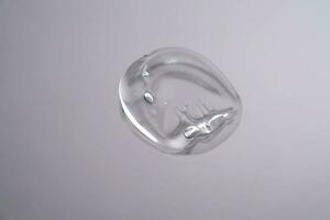 Drop of cosmetic transparent gel on a grey background. The texture of the serum, heir gel or hyaluronic booster. photo