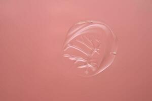 Drop of cosmetic transparent gel on a pink background. The texture of the serum, heir gel or hyaluronic booster. photo