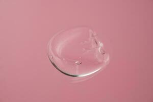 Drop of cosmetic transparent gel on a pink background. The texture of the serum, heir gel or hyaluronic booster. photo