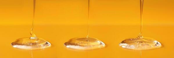 Three drops of body gel or shampoo pouring from above on a yellow saturated background. Banner. photo
