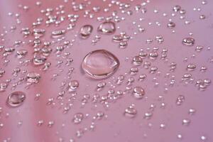 A large drop and splashes of micellar water on a pink background. photo