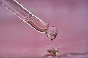 Dropper with serum or cosmetic oil on a pink background. photo