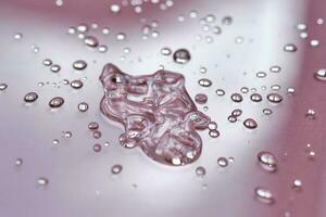 A large drop and splashes of micellar water on a pink background. photo