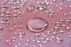 A large drop and splashes of micellar water on a pink background. photo