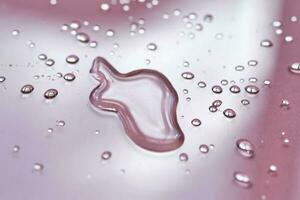 A large drop and splashes of micellar water on a pink background. photo