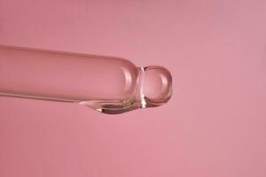 Dropper with serum or cosmetic oil on a pink background. photo