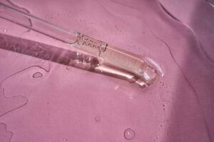 Dropper with serum or cosmetic oil on a pink background. photo