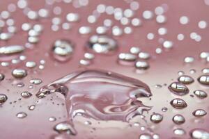 A large drop and splashes of micellar water on a pink background. photo