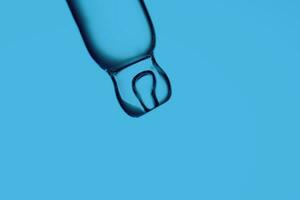 Pipette with a drop of cosmetic product on a blue background. photo