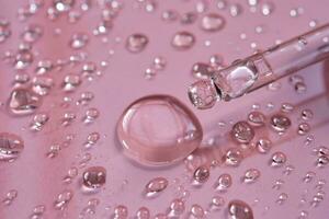 Pipette, drop and splashes of micellar water on a pink background. photo