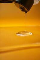 A drop of body gel or shampoo pouring from above on a yellow saturated background. photo