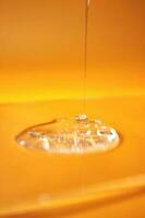 A drop of body gel or shampoo pouring from above on a yellow saturated background. photo