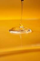 A drop of body gel or shampoo pouring from above on a yellow saturated background. photo