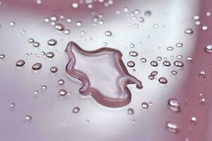 A large drop and splashes of micellar water on a pink background. photo