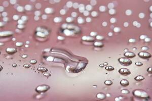 A large drop and splashes of micellar water on a pink background. photo