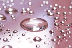 A large drop and splashes of micellar water on a pink background. photo
