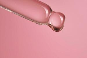 Dropper with serum or cosmetic oil on a pink background. photo