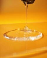 A drop of body gel or shampoo pouring from above on a yellow saturated background. photo