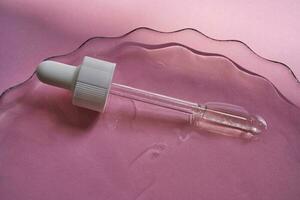 Dropper with serum or cosmetic oil on a pink background. photo