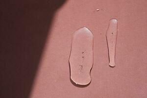 Two elongated drops of cosmetics or perfume of a plant on a pink background. photo