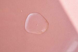 A drop of cosmetics or perfume on a pink background. photo