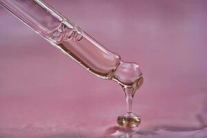 cuentagotas con suero o cosmético petróleo en un rosado antecedentes. foto