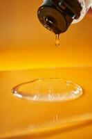 A drop of body gel or shampoo pouring from above on a yellow saturated background. photo