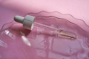 Dropper with serum or cosmetic oil on a pink background. photo