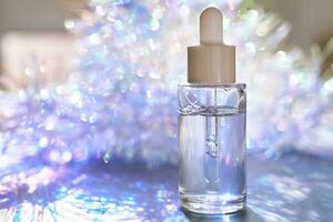 A bottle of serum with a pipette in tinsel in a Christmas theme in purple shades. photo