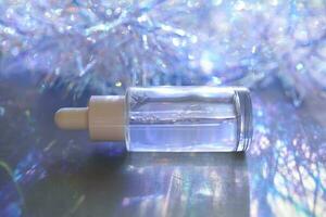A bottle of serum with a pipette in tinsel in a Christmas theme in purple shades. photo