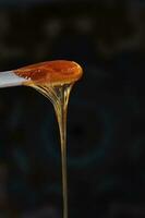 Sugaring paste drips from a wooden stick on a dark background. photo