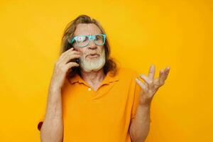 Senior grey-haired man wearing blue glasses yellow shirt talking on the phone isolated background photo