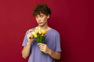 young guy holding a yellow bouquet of flowers purple t-shirts red background unaltered photo