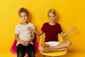 two joyful children childhood sitting on chairs together on colored background photo