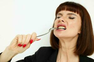 photo pretty woman in a black jacket a knife and a fork near the face light background