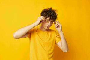 Young curly-haired man yellow t-shirt glasses fashion hand gestures isolated background unaltered photo