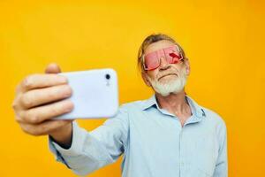 elderly man in red glasses with telephone yellow background photo
