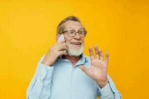 Photo of retired old man gray beard with glasses talking on the phone yellow background