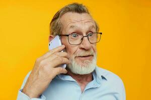 Senior grey-haired man in a blue shirt and glasses talking on the phone isolated background photo