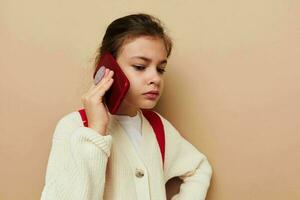 Portrait of happy smiling child girl with phone posing red backpack isolated background photo