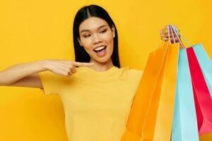 woman with Asian appearance in a yellow T-shirt with multicolored shopping bags yellow background unaltered photo