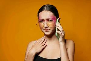 joven hermosa mujer con un teléfono en mano brillante maquillaje posando Moda emociones amarillo antecedentes inalterado foto